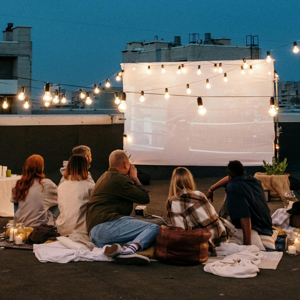 Group of friends enjoying an outdoor movie night on a rooftop, surrounded by string lights.